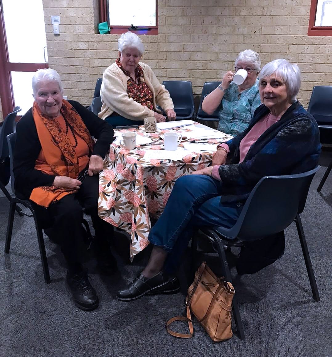 Four senior women sitting around a table enjoying hot drinks