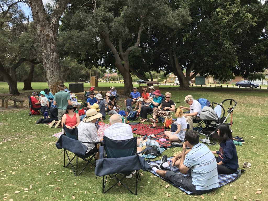 A large group of people sitting in a park enjoying a picnic